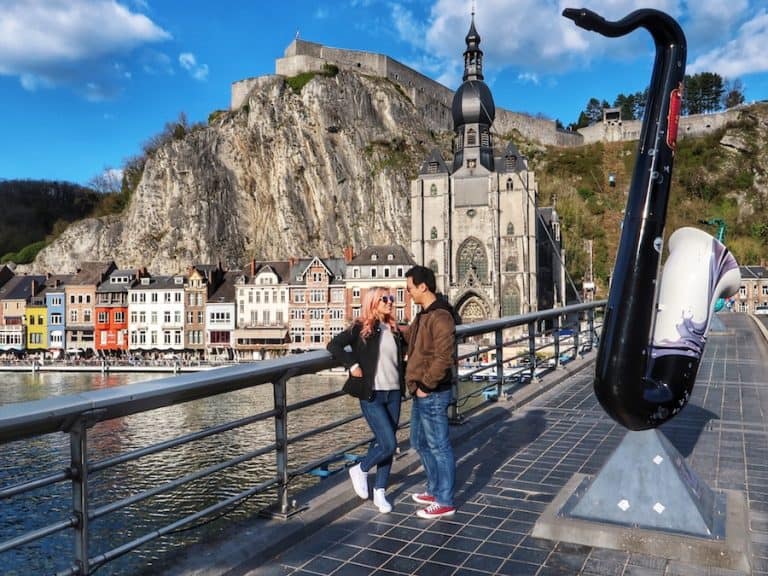 Cover image for Best Things To Do In Dinant article - Jeff and Zuzi standing on the Charles de Gaulle in Dinant, Belgium. The Notre Dame de Dinant and Citadel in the background