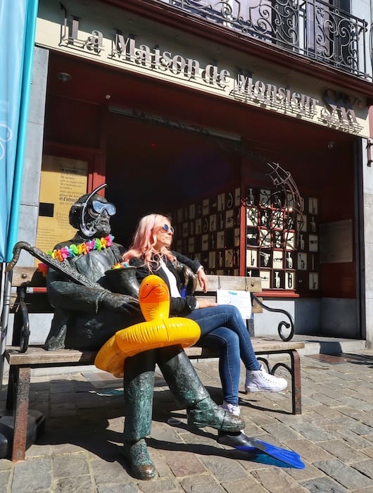 Zuzi is sitting outside La Maison de Monsieur Sax on a bench with a statue Adolphe Sax