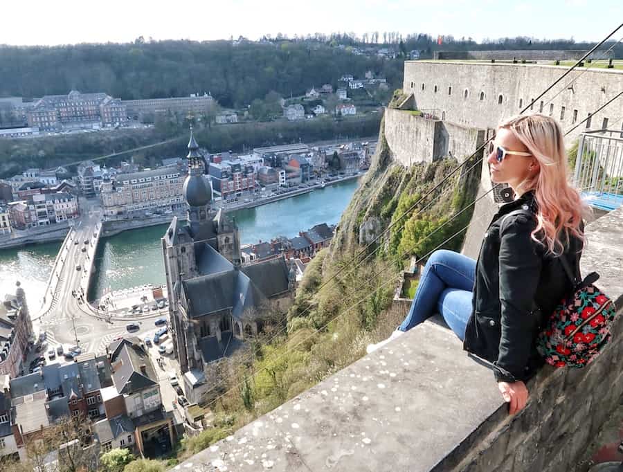 Zuzi sits on a wall at the top of the Citadelle de Dinant, staring across the city with the cathedral and the River Meuse below