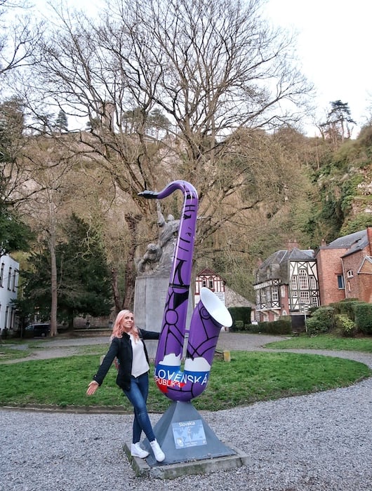 Zuzi stands next to a giant saxophone decorated with in purple and has a Slovakian flag at the bottom