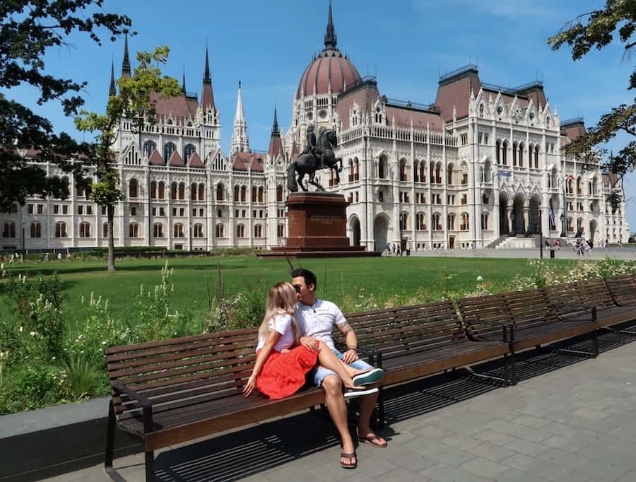 Jeff and Zuzi kiss on a bench in front of the Hungarian Parliament Building in Budapest