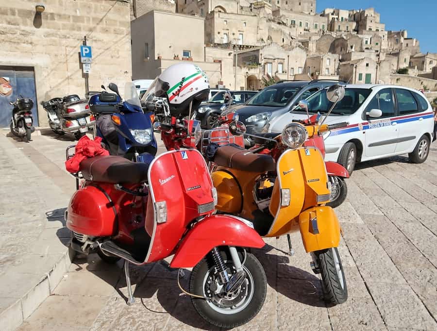 An orange and a red Vespa in the a car park in Matera