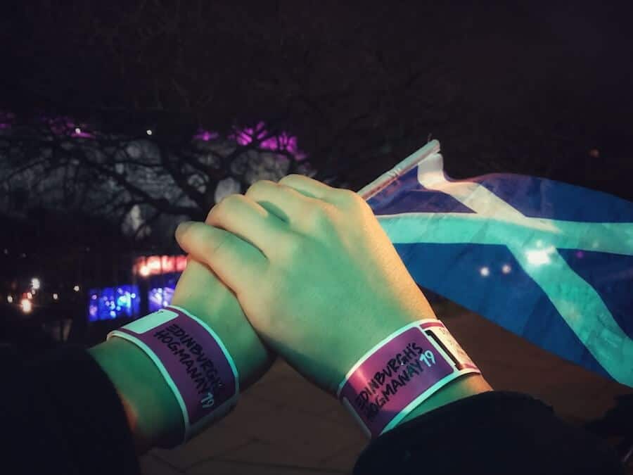 Images of Jeff and Zuzi's hands wearing their Hogmanay wristbands and carrying a mini Scotland flag