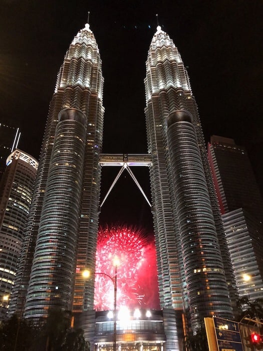 Image of the Petronas Towers. Twin towers in Kuala Lumpur. It is lit up at night and there are some fireworks being set off inbetween