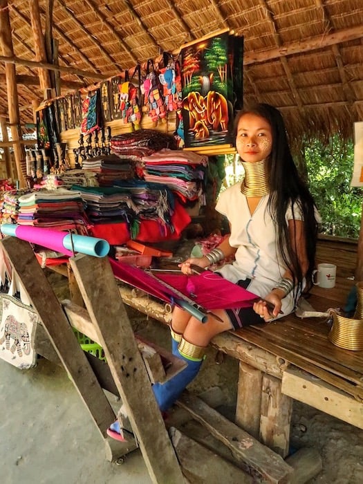 A girl from the Karen Longneck Hill tribe in Thailand sits and knits