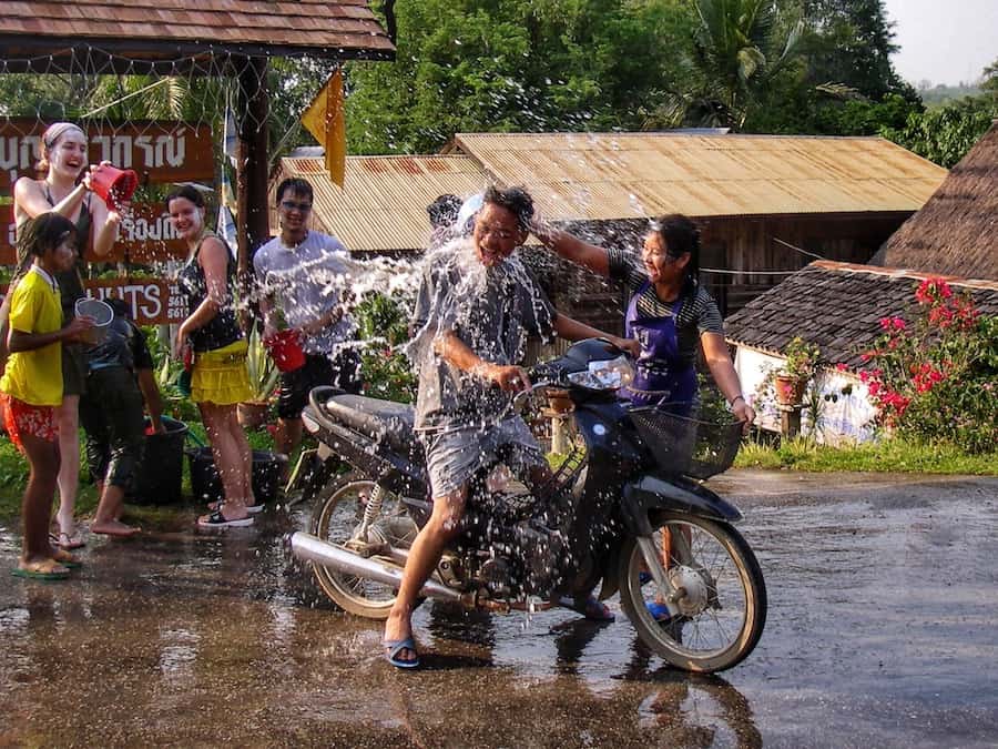 Local children splash a man on a scooter with water in a village in Thailand