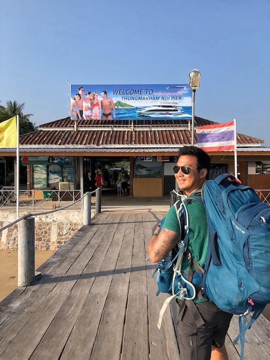 Jeff is carrying his backpack and walking on the pier in Thailand