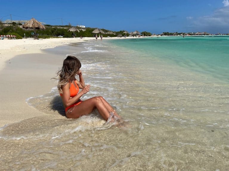 Zuzi sitting on the sand and clear, blue water on Baby Beach Aruba