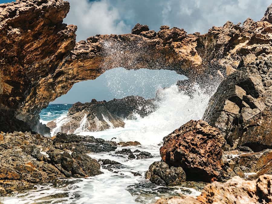 Image of a natural bridge in Aruba where the waves crash against a rocky archway 