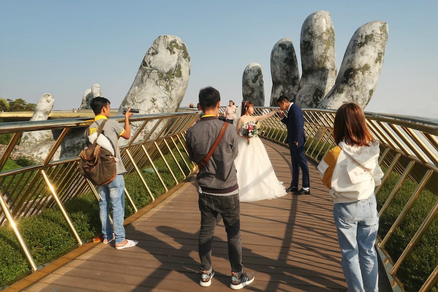 Image of a bride and groom having a wedding shoot with photographers on the golden hands bridge vietnam