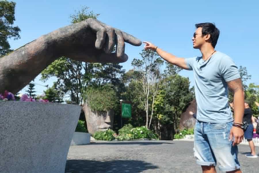 Jeff is touching fingers with a large model of a stone hand at Ba Na Hills Resort in Vietnam