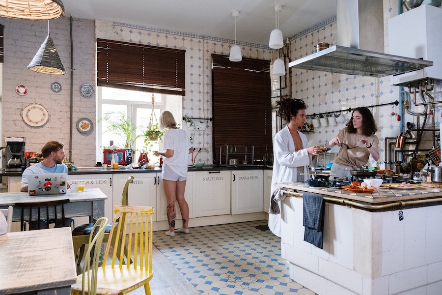 Image of several people sharing a communal kitchen. One person is on his laptop on the table