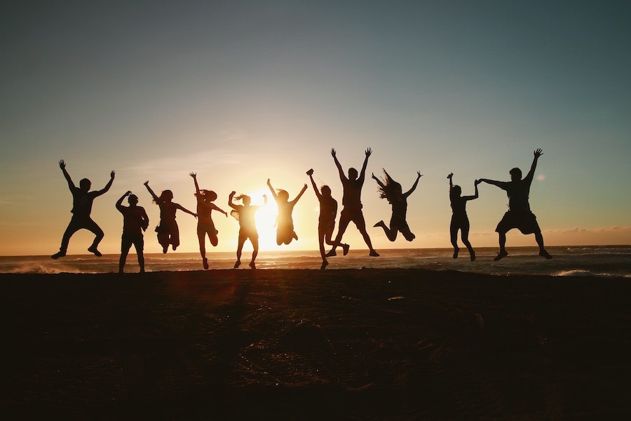 A silhouette image of many people jumping in front of a sunset