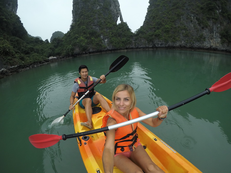 Image of a couple on a yellow kayak in Ha Long Bay Vietnam. Concluding photo for is Vietnam worth visiting post. The water is green and there are pinnacles in the background