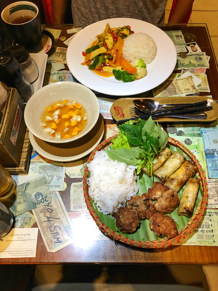 Image of Bun Cha, a dish from Vietnam showing fried meat and spring rolls on the plate with rice and vegetables on another. The food makes Vietnam worth visiting