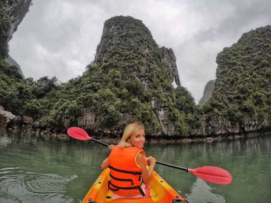 Zuzi is in a kayak in Ha Long Bay with large stone pinnacles in the background