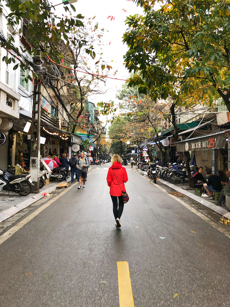 Zuzi is wearing a red jacket and walking down a rainy street in Hanoi