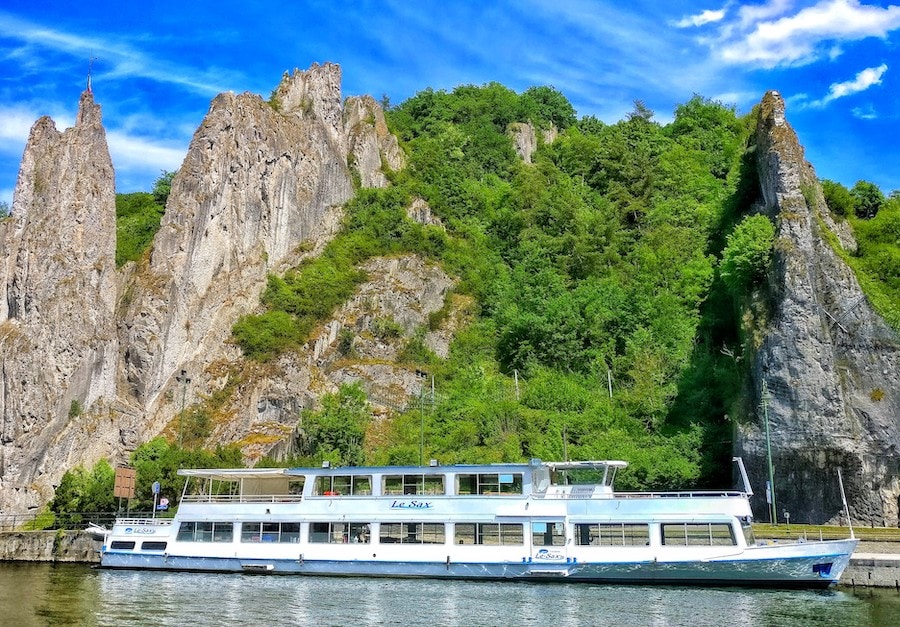 Image of an small tour boat passing a rock formation on the River Meuse in Dinant, Belgium