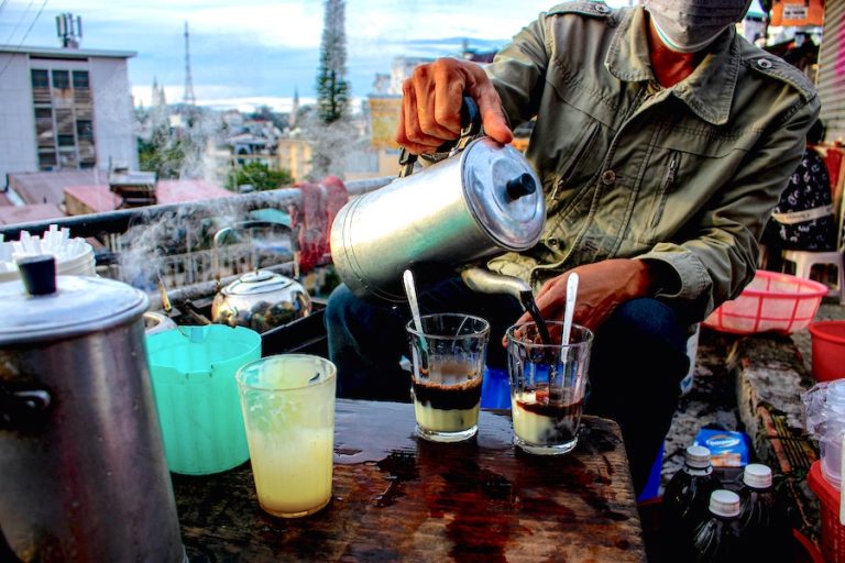 Cover image for Best Coffee In Vietnam where a man pours coffee into glasses on a rooftop in Vietnam