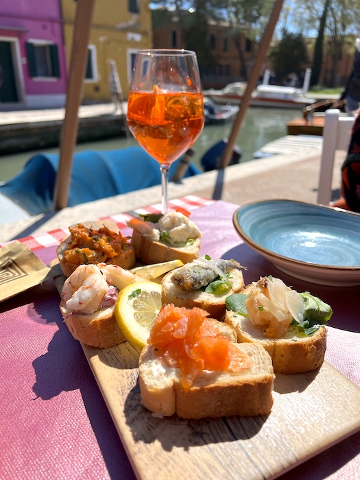 Image of some food, mainly bread with fish, and a glass of Aperol spritz