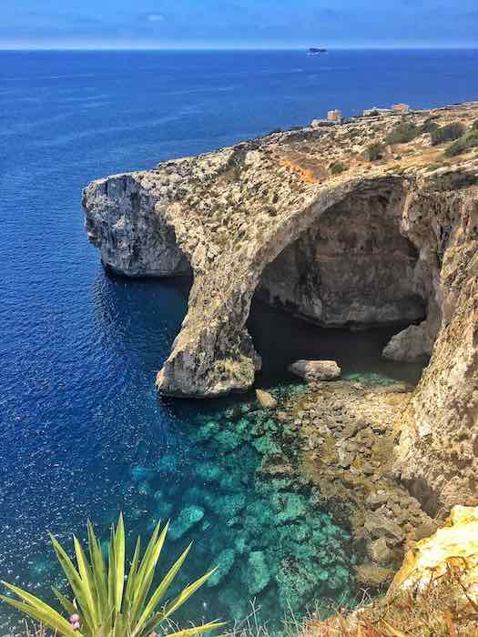 the rocky cliff of the Blue Grotto in Malta with the turquoise sea in the foreground