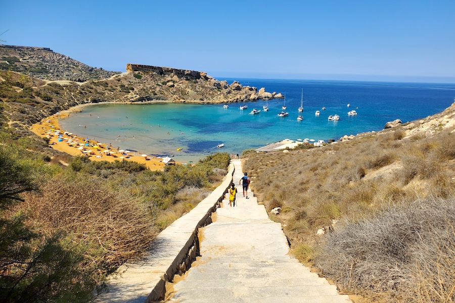 View of Għajn Tuffieħa, Malta, with tourists walking down the stone steps towards the sand beach and turquoise water