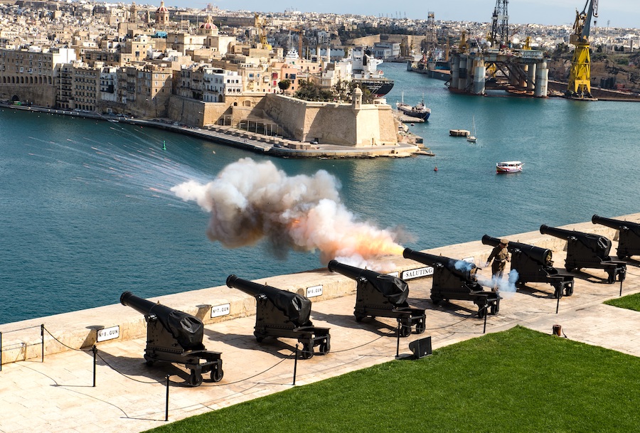 a row of cannons along a fort in Valletta with one being fired and smoke coming out