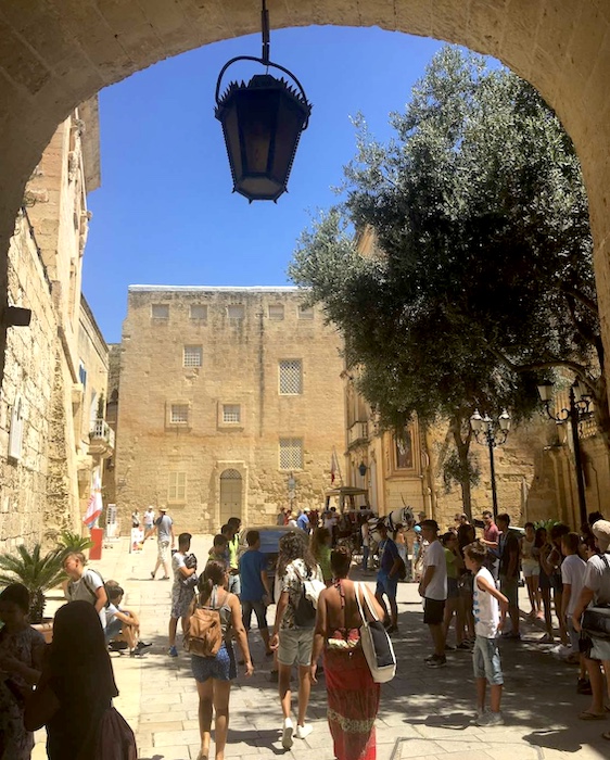 tourists walk through an arch in Mdina, Malta