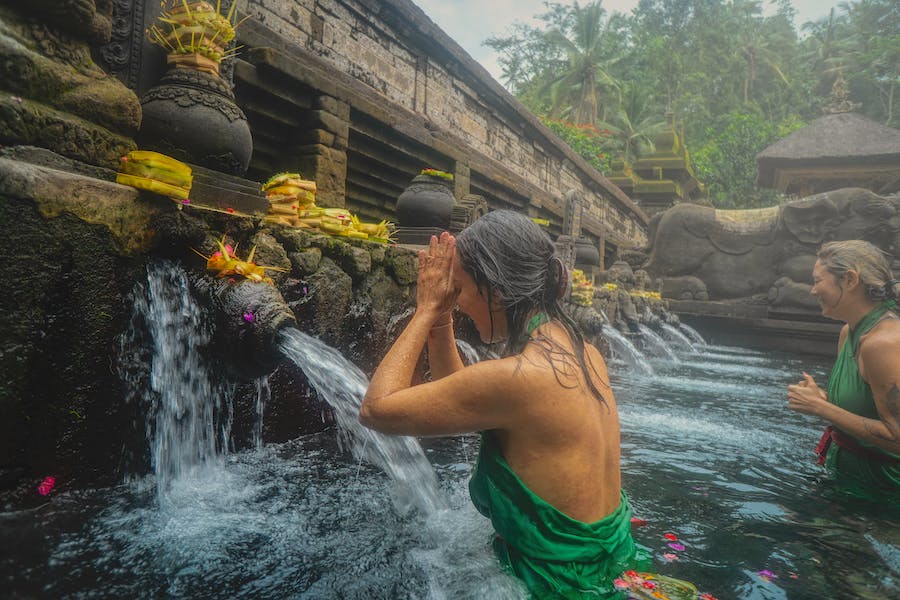 Woman in green is washing in a Bali local ritual with traditional fountains