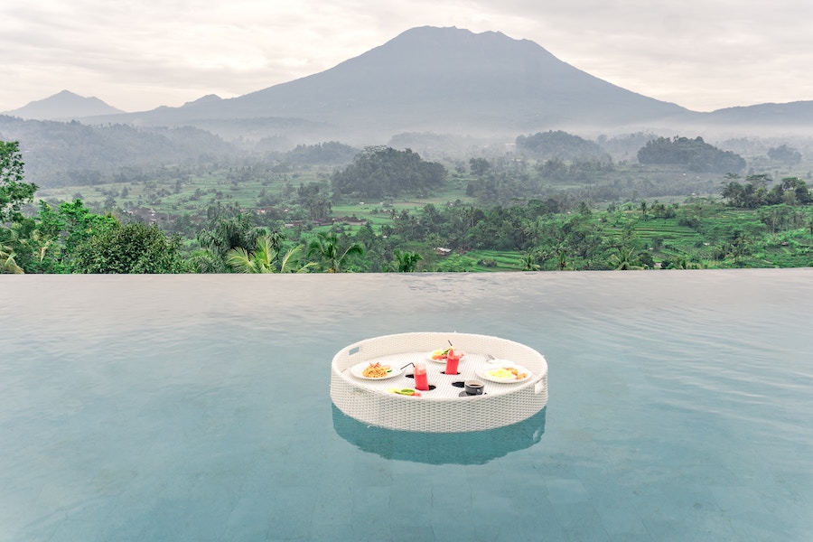 A plate with food floats in a pool overlooking rice terraces and the mountain in Bali.