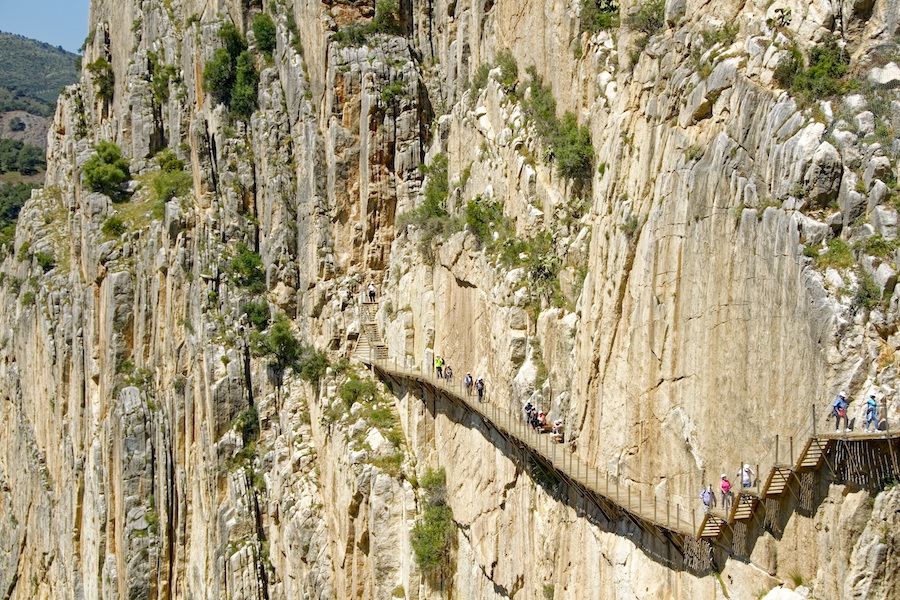 sheer vertical rock cliff face with a small path tourist are taking along the middle