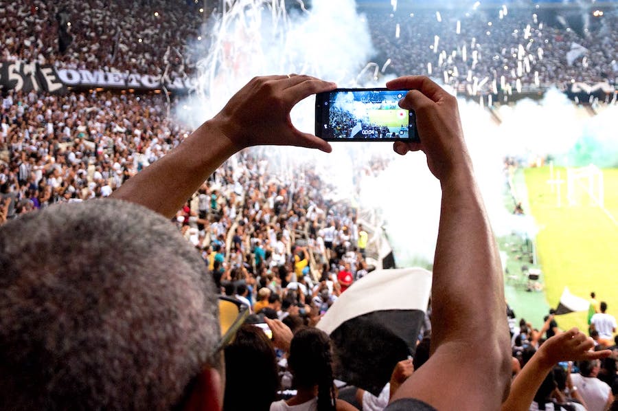 A man is recoding an image of a football game on his mobile phone in a packed stadium