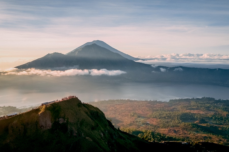 Mount Batur in Bali is shrouded in cloud and mist with tourists in the foreground for scale.