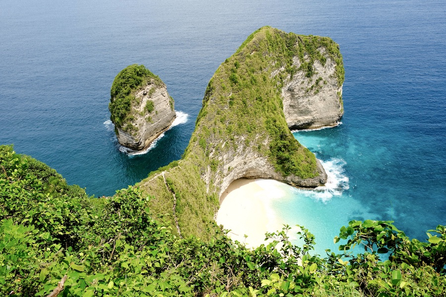 A secluded white beach in Bali surrounded by grassy cliffs and the sea