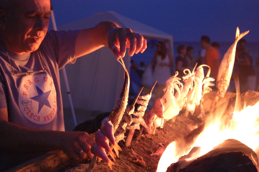 A man is placing various seafood onto skewers with the fire burning on the grill