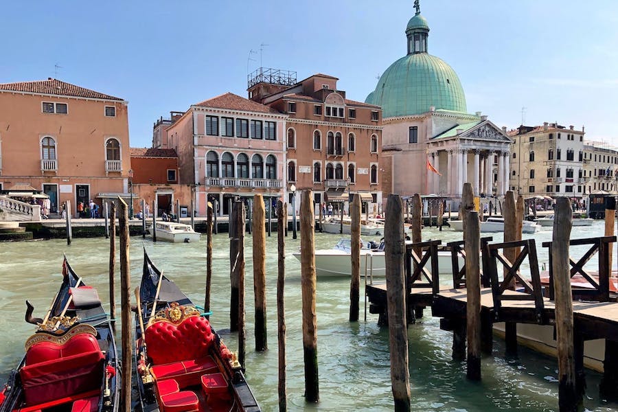 The Grand Canal in Venice with gondolas in the water as well as many poles for tying up boats and a dome in the background