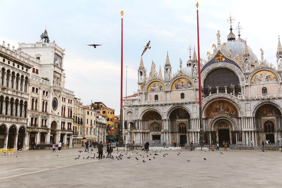 White stone church of St. Marks Basilica in Venice with people in the square feeding pigeons