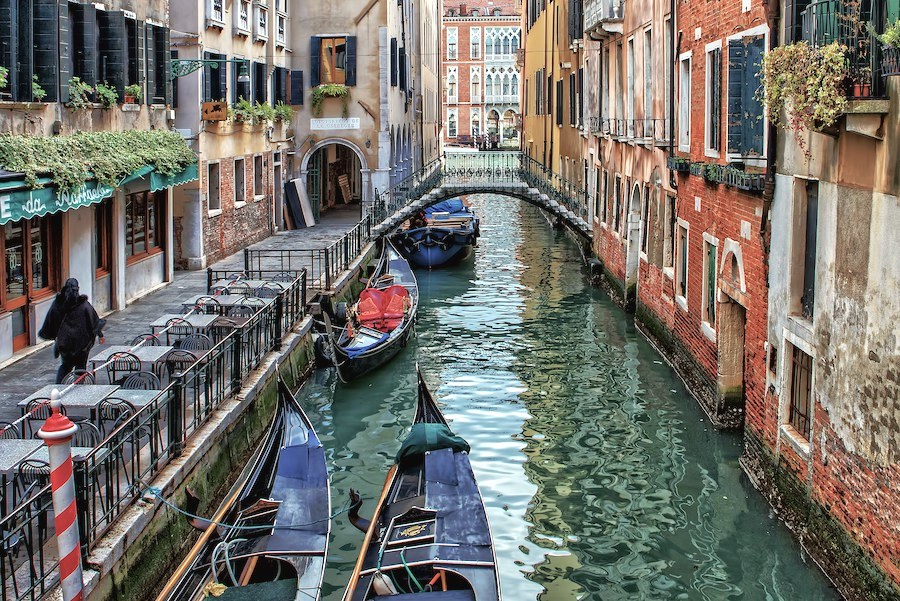 Gondolas on the canals in Venice with houses either side of the canal and a bridge up ahead