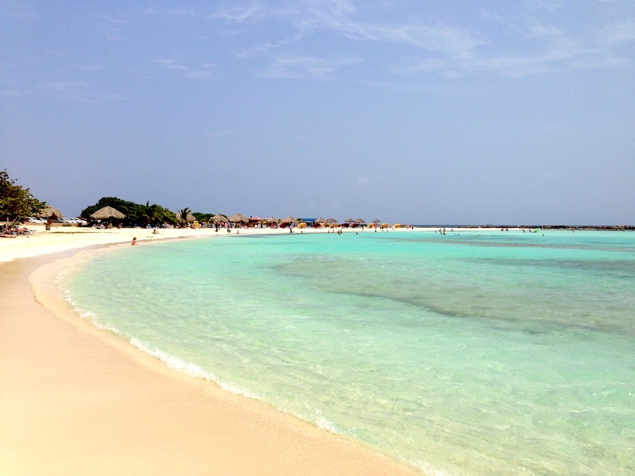 The very turquoise water at Baby Beach in Aruba with some grass huts far in the distance.