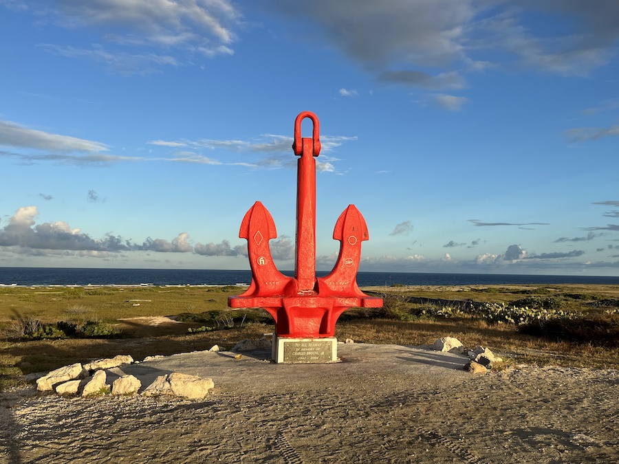 Tall red anchor standing upright in Aruba with the coast on the far distance.