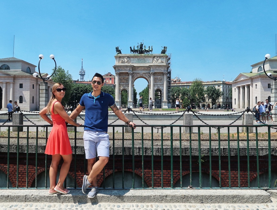 Jeff and Zuzi stand against as railing in Milan with a stone arch in the background - the Arco della Pace