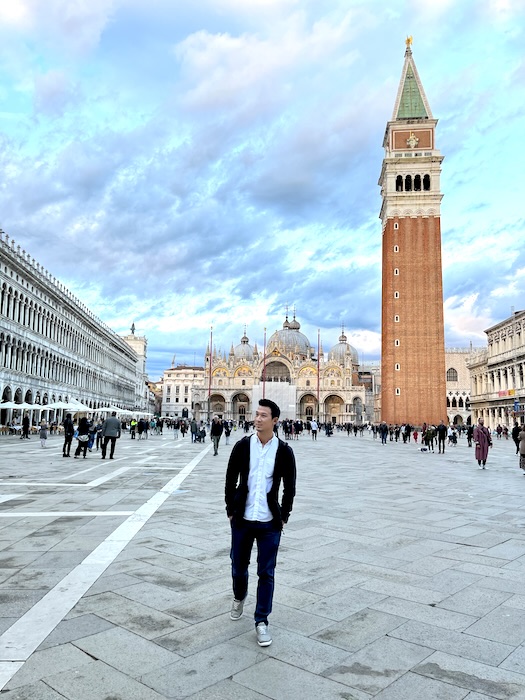 Jeff is walking in St Marks square in Venice with the Bell Tower behind