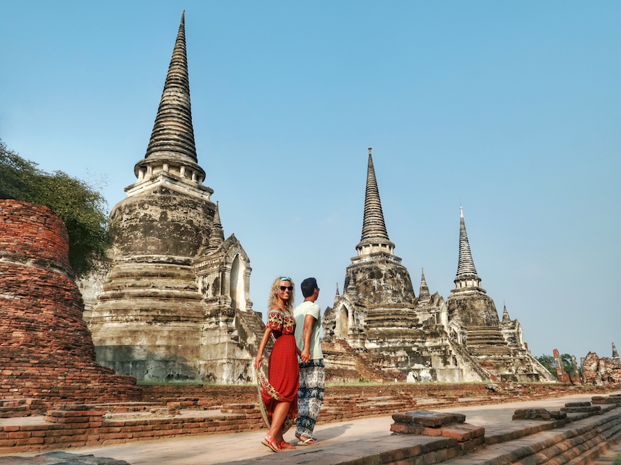 Two tourists visiting Wat Phra Si Sanphet during a day trip to Ayutthaya from Bangkok, standing in front of the iconic chedis in Ayutthaya Historical Park, Thailand.