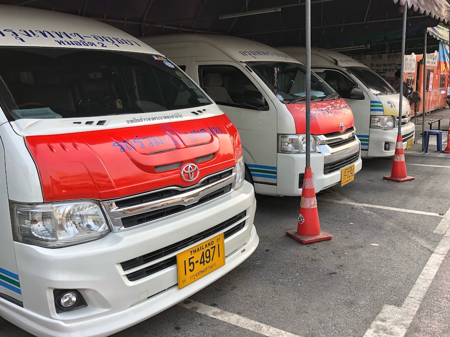 Row of white and red minivans at Mo Chit Bus Terminal in Bangkok, Thailand, used for public transport to Ayutthaya, with Thai writing on the windshields and yellow licence plates.