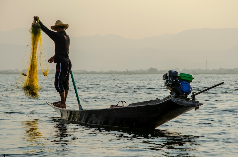 Fisherman balancing on a boat on Inle Lake in Myanmar using a traditional fishing net