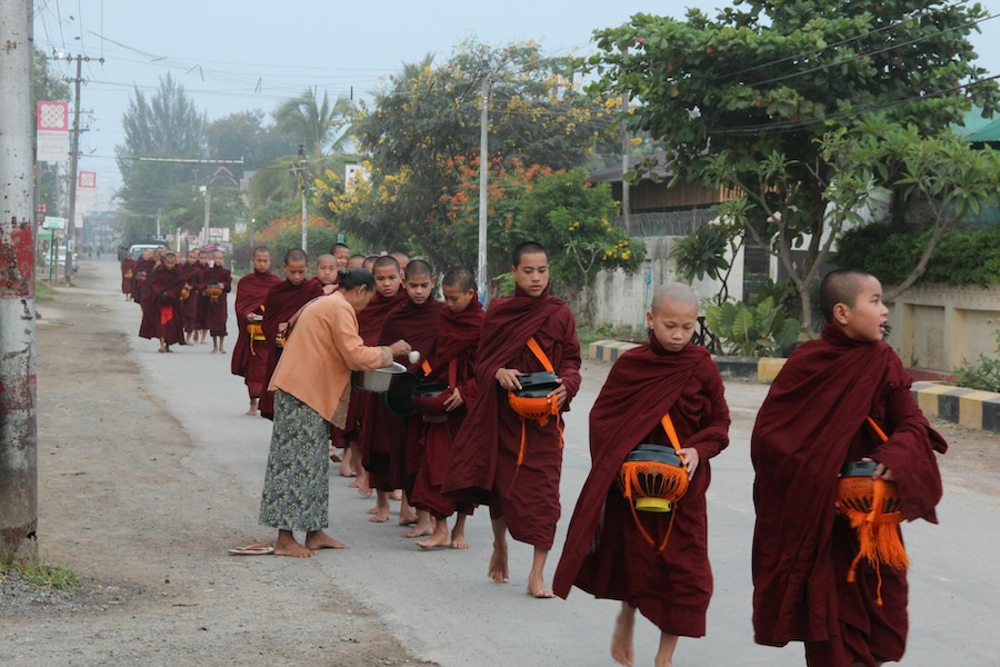 Buddhist monks walking barefoot along a quiet street in Myanmar during morning alms