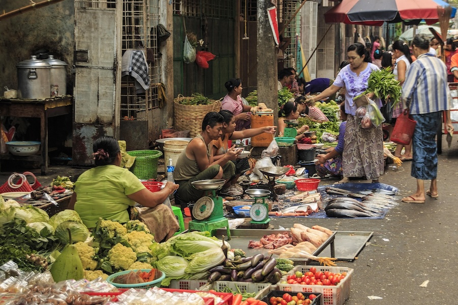 Busy local street market in Myanmar with fresh vegetables, fish and vendors selling food